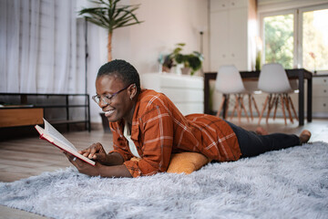 Young woman lying on carpet reading a book at home