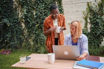 Two businesswomen working outdoors with a laptop and having a discussion