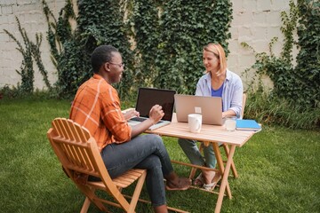 Two businesswomen working outdoors with laptops, enjoying summer day in the garden