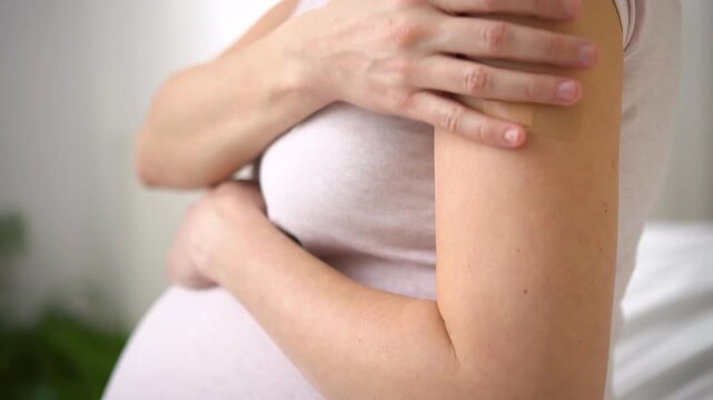 Masked expecting mother with vaccination bandage on forearm. Thoughtful moment of maternal health protection through scheduled immunization program.