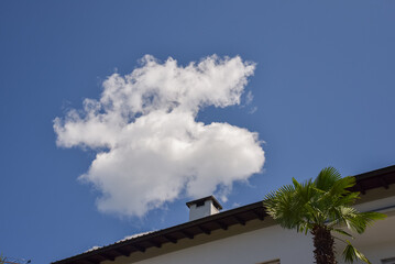 fluffy white cloud appears to rise like smoke from a chimney against a vivid blue sky, creating a...