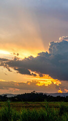 Sunset with intense golden rays shining through dramatic clouds over distant hills