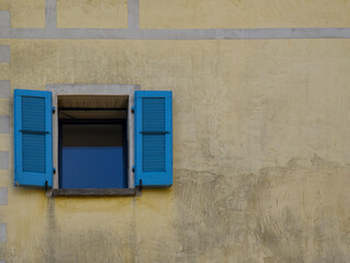 single open window with bright blue wooden shutters contrasts vividly against a weathered yellow...