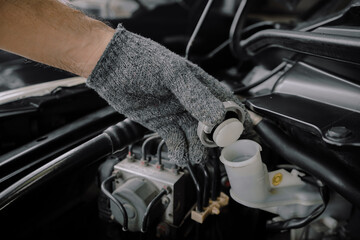 Close-up of mechanic's hand opening brake fluid tank cap to check level or replace in engine...