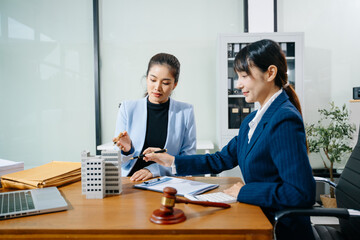 Two businesswomen discussing real estate contract with legal documents, gavel, and property model....