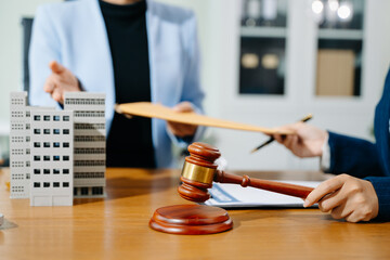 Businesswoman hands over legal envelope beside building model, gavel, and contract. Real estate...