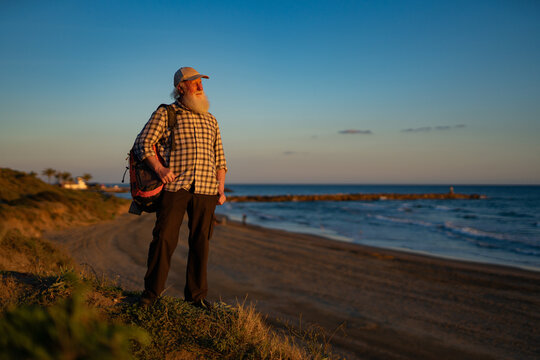 Senior Man with Long White Beard Hiking Along Coastal Cliffs at Sunset
