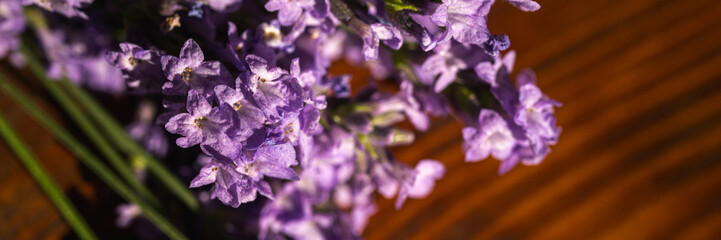Fresh lavender bouquet on a rustic wooden background in warm sunlight. Aromatherapy, spa, and wellness concept. Banner format with copy space, horizontal photo