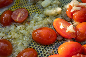 Close-up of cherry tomatoes and garlic sautéing in olive oil with herbs. Preparing a delicious Italian pasta sauce. Mediterranean cuisine concept