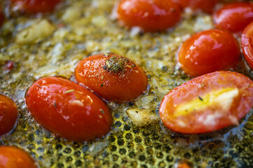 Close-up of cherry tomatoes and garlic sautéing in olive oil with herbs. Preparing a delicious Italian pasta sauce. Mediterranean cuisine concept