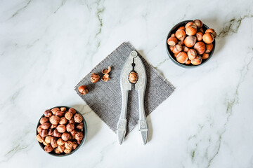 Symmetrical flat-lay: twin bowls of whole and shelled hazelnuts flank ornate metal nutcracker on...