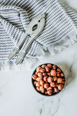 Minimal rustic composition — metal nutcracker resting on woven cotton cloth next to bowl of dried...