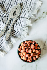 Minimal rustic composition — metal nutcracker resting on woven cotton cloth next to bowl of dried...
