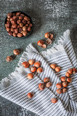 Overhead composition: hazelnuts spilling across checked kitchen towel on weathered slate...