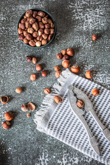 Vertical flat-lay of mixed whole and shelled hazelnuts with ornate nutcracker on grey textured...
