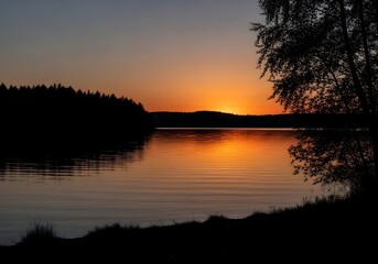 Fototapeta premium Scenic sunset reflecting on the calm lake water with silhouette of trees in the evening