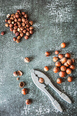 Overhead layout: separated piles of roasted and raw hazelnuts flank metal nutcracker on distressed...