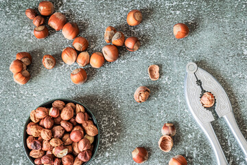 Overhead layout: separated piles of roasted and raw hazelnuts flank metal nutcracker on distressed...