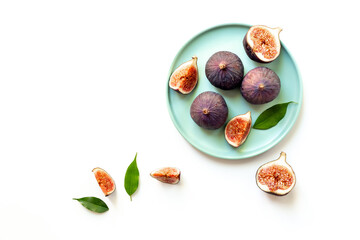 Purple ripe figs and slices with leaves on a plate top view on a white background