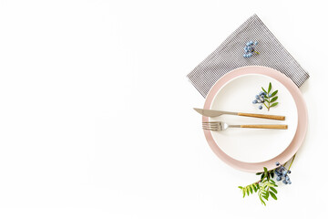 Beautiful minimalistic table setting with empty plate, cutlery and napkin - green leaves and...