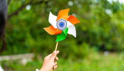 A hand holds a pinwheel with the Indian flag's tricolor design against a lush green background.