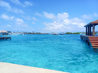 Crystal-clear turquoise waters extend from a wooden pier with stairs leading into the sea, depicting a tropical waterfront resort. Related to  luxury travel, beach vacations, tropical destinations	