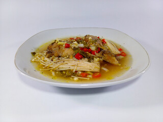 A hearty stew, Mechado Yucateco, is served in a white, slightly irregular-shaped bowl. The dish features tender meat chunks, enoki mushrooms, and a colorful garnish of finely diced red chilies