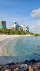 Idyllic tropical beauty of Maafushi Island, Maldives. Crystal-clear turquoise ocean water against a pristine white sandy beach, lined up by modern multi-story hotel buildings and beachfront amenities	