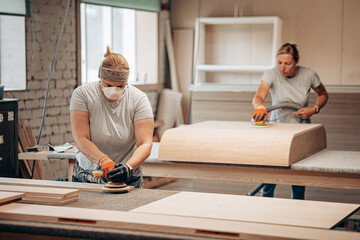 Two Women Sanding Wooden Surfaces in Carpentry Workshop