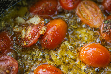 Close-up of cherry tomatoes and garlic sautéing in olive oil with herbs. Preparing a delicious Italian pasta sauce. Mediterranean cuisine concept