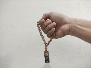 Close-up of a hand holding wooden prayer beads with a small souvenir pendant. Ideal for spirituality, meditation, religion, or cultural concepts. Neutral background for easy design use.