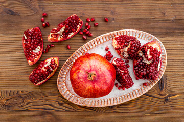 Fresh ripe pomegranate with cut in half and pieces on plate to eat, top view.
