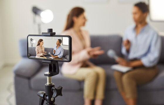 Video interview with influencer, live podcast recording for social media with smartphone camera on tripod. Journalist and guest sitting on couch to record dialogue. Content creation, vlog concept - Powered by Adobe