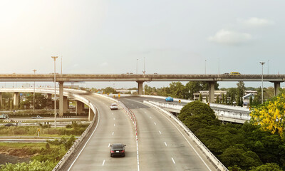 Dramatic aerial view of elevated roads and traffic junction in suburb area of Bangkok with beautiful view of countryside atmosphere during sunny day.