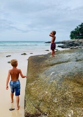 Two preschool boys enjoy a sunny day on a tropical beach. Sandy shore, clear water, and large rocks...