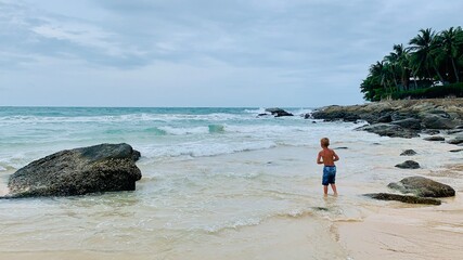 A boy runs along the sandy beach, splashing in gentle waves. Joyful summer moment, carefree...