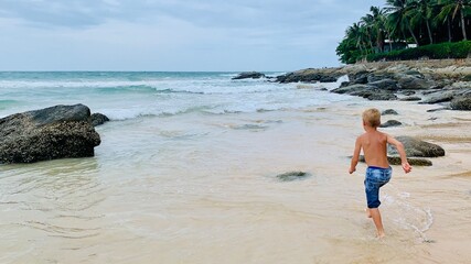 A boy runs along the sandy beach, splashing in gentle waves. Joyful summer moment, carefree...