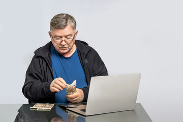 Senior Man Counting Euro Banknotes at Home Using Laptop