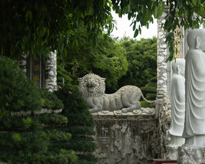 Stone Lion Statue and Buddha Figures at Ornate Temple Entrance in Lush Garden

