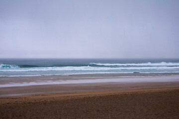 Waves rolling onto the sandy shore of Zarautz beach under a cloudy sky during early morning
