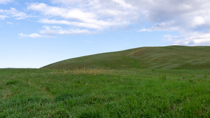 Long mountains. Lush green hillside under a bright blue sky with scattered clouds, showcasing the beauty of nature and the tranquility of open landscapes in a serene environment