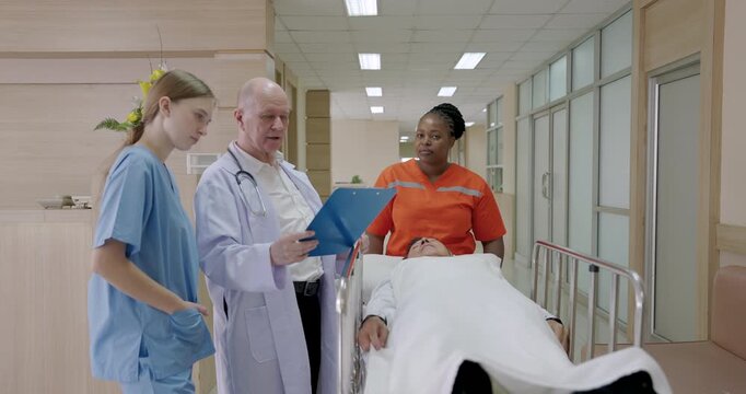 Medical team moving patient on stretcher through hospital hallway during emergency situation as doctors and nurses discussing chart in slowmotion showing urgent teamwork and healthcare response