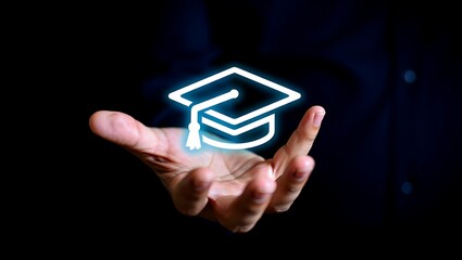 Hand holding glowing graduation cap symbol on dark background