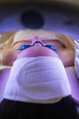 Vertical close-up of woman receiving blue led phototherapy wearing protective goggles calming...