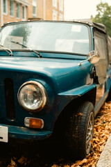 Fototapeta premium Front close-up of a vintage blue convertible parked on a leaf-covered street in Chiswick, West London