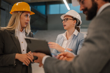 Engineers and architects discussing building plans on tablet in office meeting
