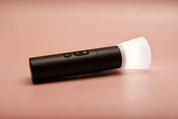 A flashlight for studio lighting. Compact flashlight for the photographer. A flashlight on a pink background.
