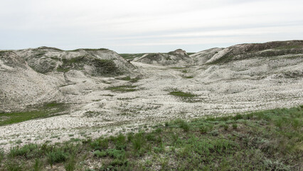 Pokrovsky Cretaceous mountains. Expansive arid landscape features rolling hills and sparse vegetation, showcasing unique geological formations and textures under a cloudy sky