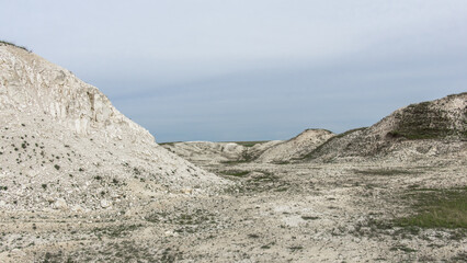 Pokrovsky Cretaceous mountains. Expansive barren landscape with white rocky hills and sparse vegetation under a cloudy sky, showcasing the beauty of natural geological formations