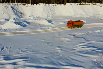 orange dump truck in winter in a snow-covered sand quarry.